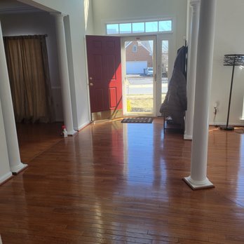 MaidPro - Door left open when they left - A spacious house interior with polished hardwood floors, white walls, and large windows allowing natural light. The red front door is open, revealing a street view outside. - Home Cleaning Near Me - Frederick, Maryland