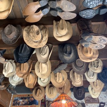 Mother Lode Mercantile - This was in the saloon!! Hats and boots hanging from the ceiling. - Multiple cowboy hats and boots are hanging from a wooden ceiling in a store, with some hats decorated with handwritten messages, dates, and names. The display includes different styles and colors, with a vintage and rustic ambiance. The store features wooden beams, a hanging lamp, and various signs and photographs on the walls, emphasizing a western or cowboy theme. - Candy Stores Near Me - Apache Junction, Arizona