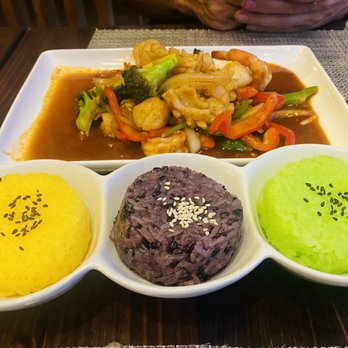 Thai Table - Seafood chili paste with tricolor sticky rice - A plate of Thai cuisine featuring three types of rice—yellow, purple, and green—served in small bowls, with a stir-fried seafood and vegetable dish in the background. - Thai Near Me - Frederick, Maryland