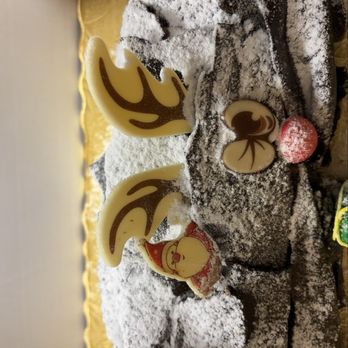 Bake - Yule log - A festive cake decorated with reindeer antlers, a Santa face, and holiday candies, dusted with powdered sugar, on a table. - Bakeries Near Me - Summit, New Jersey