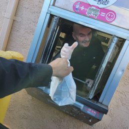 Arrrggghhh yummy - A man is leaning out of a drive-thru window, smiling and giving a thumbs-up while receiving a bag of food from an employee.
