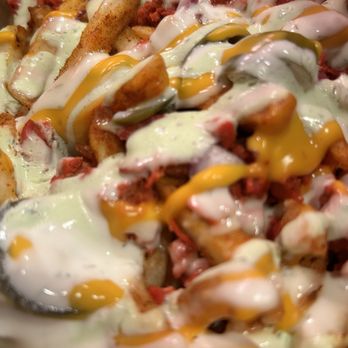 Big Red Halal - A close-up of loaded fries with melted cheese, white and yellow sauces, and bacon bits, served at Big Red Halal in Springfield, VA. - Afghan Near Me - Springfield, Virginia