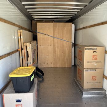 Heroic Movers - A moving truck interior with cardboard boxes, wooden furniture, and packing supplies, ready for transport. - Movers Near Me