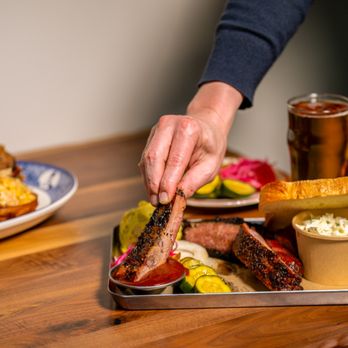 Founding Farmers & Distillers - A hand reaches in to pick up a glazed spare rib from a metal BBQ tray loaded with sliced smoked brisket, bread and butter pic... - Breakfast & Brunch Near Me - Washington, DC, District of Columbia Founding Farmers & Distillers - A hand reaches in to pick up a glazed spare rib from a metal BBQ tray loaded with sliced smoked brisket, bread and butter pic... - Breakfast & Brunch Near Me - Washington, DC, District of Columbia