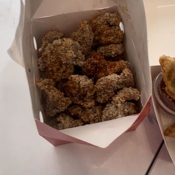 Tsaocaa - St Johns - A paper container filled with fried chicken pieces is positioned on a white surface. The chicken appears crispy and seasoned. Part of a drink in a plastic cup and another food item are visible to the right. The image is taken from above, showing the food presentation and setting. - Desserts Near Me - Saint Johns, Florida