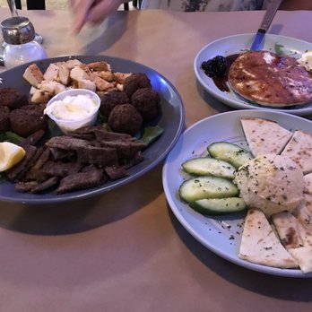 Cedar Tree - Saganaki Cheese in the background, Keftedes, chicken, falafel, chicken on left, humus on right. - Three plates of Mediterranean cuisine are shown: one with falafel, grilled meat, and bread; another with a grilled fish fillet, lemon, and sauce; and a third with pita, cucumber slices, and hummus. - Mediterranean Near Me - River Vale, New Jersey