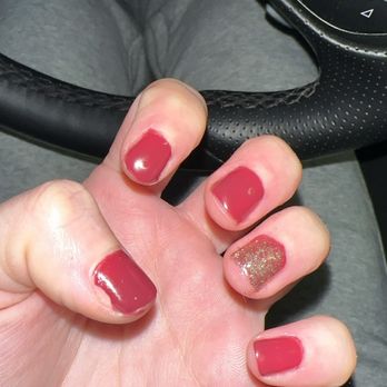Luxury Nails and Spa - The image shows a close-up of a person's left hand with painted nails, featuring a mix of solid pink and glitter nail polish. The hand is positioned near the steering wheel of a vehicle, with the dashboard and control buttons visible in the background. The person is wearing gray clothing, and the photo captures the interior of the car, including the steering wheel and part of the dashboard. - Hair Removal Near Me - Albuquerque, New Mexico