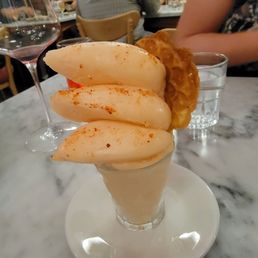 Melon sorbet - A dessert featuring melon sorbet garnished with paprika, served with a fried item, alongside a glass of red wine on a marble table.