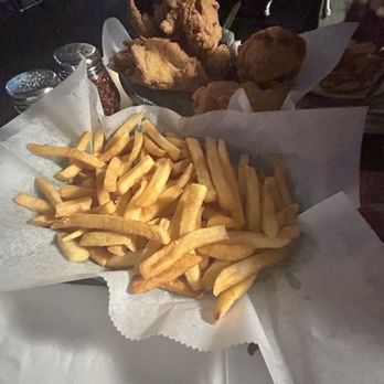 Frankie V's Bar & Grill - Fries - A basket of French fries served on white paper in a restaurant setting, with fried chicken pieces visible in the background. - Italian Near Me - Whiting, Indiana