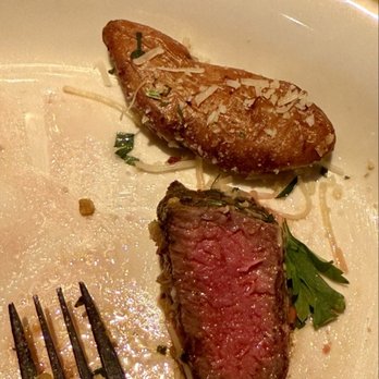 Antico Posto - My wife called it a perfectly medium Strip Steak Giardiniera* - A white ceramic plate contains a partially eaten medium-rare steak with a pink interior and a seared exterior. Next to the steak is a roasted potato topped with grated cheese and small herbs. A fork rests on the plate, and some juices and crumbs are visible on the surface. The setting suggests a dining experience at a restaurant, possibly Italian, given the context of the review. - Italian Near Me - Oak Brook, Illinois