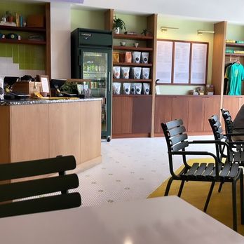 Catalog Coffee - Order counter - A cafe interior featuring a counter with a refrigerator, shelves with coffee bags, and a menu board. Seating includes black chairs and a white table. - Breakfast & Brunch Near Me - Baltimore, Maryland