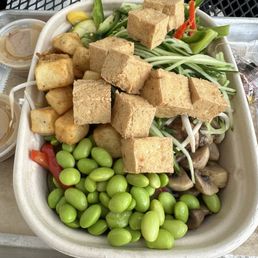 A mixed vegetable salad featuring tofu cubes, edamame, mushrooms, and sliced vegetables, served with dipping sauces.