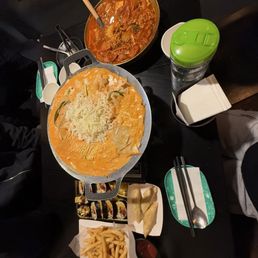Rose Tteokbokki - A table features Korean cuisine such as rose tteokbokki, army stew, French fries, and various side dishes, with utensils and drinks.
