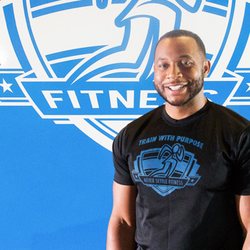 Never Settle Fitness - Nate posing in front of the Never Settle Fitness logo at our Castleton gym.