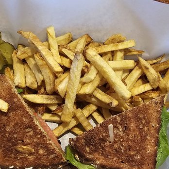 Bajis Cafe - A plate with French fries, sliced pickles, and a sandwich with lettuce, served on parchment paper on a wooden table. - Breakfast & Brunch Near Me - Mountain View, California