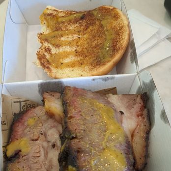 Wonder Framingham - Texas Brisket sandwich - The image shows a boxed meal containing slices of cooked brisket with melted cheese and a drizzle of sauce, placed on a piece of branded paper. A slice of garlic bread with seasoning and oil is positioned above the meat. The meal is on a table with a glass of water and a napkin nearby, suggesting a casual dining setting. - Food Delivery Services Near Me - Framingham, Massachusetts