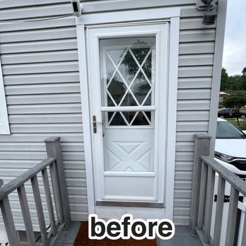 MDR Home Improvement - A white exterior door with diamond-shaped glass panels is set in a house with vinyl siding, flanked by small porch railings. - General Contractors Near Me