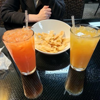 Wei-Li - Mai Tai and Bahama Momma - Two beverages, one orange and one yellow, are served in tall glasses with straws, accompanied by a bowl of chips on a black table. - Chinese Near Me - Auburn, Maine