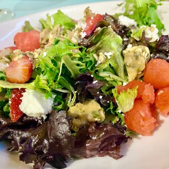 Claim 52 Kitchen - Seasonal Salad - A mixed green salad featuring various leafy greens, sliced strawberries, watermelon chunks, avocado, and crumbled cheese, served on a white plate. - Gastropubs Near Me - Eugene, Oregon