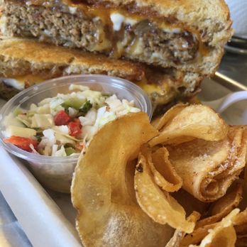 Absolutely CheeZee - Special of the Day! Meatloaf Grilled Cheese with red pepper jelly! - The image shows a meatloaf grilled cheese sandwich with toasted bread, melted cheese, and meatloaf filling. Accompanying the sandwich are crispy potato chips and a small cup of coleslaw with chopped cabbage and peppers. The meal is presented on a tray, highlighting a hearty, cheese-based sandwich with side snacks. - Soup Near Me - Ormond Beach, Florida