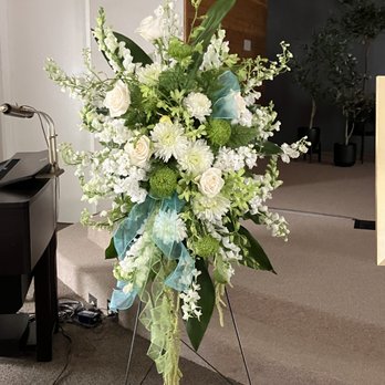 Rowlee's Buds - Standing spray in greens and white, including roses, orchids, snapdragons, cremons, another others. - Florists Near Me