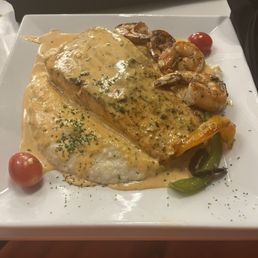 Salmon with shrimp and grits. Brunch item. - A plate of salmon with shrimp and grits, topped with a creamy sauce, accompanied by cherry tomatoes and roasted vegetables.