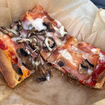 Rosetta Bakery - A slice of pizza topped with mushrooms, ham, and melted cheese on brown parchment paper. - Bakeries Near Me - Miami, Florida