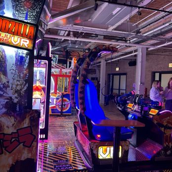 Elston Electric - Arcade - Indoor arcade with VR and traditional arcade games, including a Godzilla VR machine, illuminated with colorful neon and LED lighting. - Arcades Near Me - Chicago, Illinois