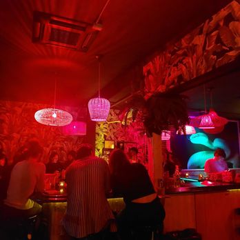 Zig Zag - A bar interior illuminated by red, pink, and blue neon lights, with patrons seated at the bar and engaging in conversation. - Cocktail Bars Near Me - Brooklyn, New York