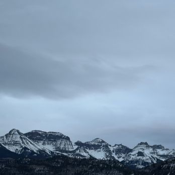 Black Bear Manor - The image depicts a mountain range with multiple peaks covered in snow, set against a sky filled with gray clouds. The mountains are part of a natural landscape, with forested slopes visible at the base. The scene emphasizes the rugged terrain and winter conditions of the area. - Bed & Breakfast Near Me - Ouray, Colorado