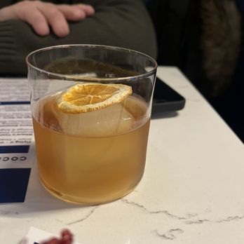 Capri Columbus - Maple old fashioned - A cocktail with a lemon slice on ice in a clear glass, placed on a white table at a bar or restaurant. - Cocktail Bars Near Me - Columbus, Ohio