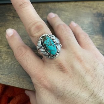 Warpath Trading Post - A person's hand is shown wearing a silver ring with a large turquoise stone, resting on a wooden surface near a keyboard. - Jewelry Near Me - Albuquerque, New Mexico