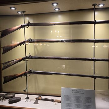 Frontier Tavern - The long rifle collection with restored tomahawk and head-batteting stone within glass, along with original arrowheads - New American Near Me - Bedford, Pennsylvania