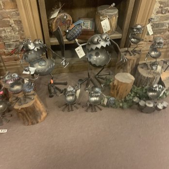 Backroads Art - Collection of metal sculptures resembling cartoonish creatures with exaggerated features, arranged on logs and the floor in front of a wooden cabinet. - Art Galleries Near Me - Weston, Missouri