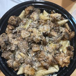Rasta Pasta with jerk chicken and shrimp. My shrimp we're on the side. - A black bowl holds pasta topped with cooked chicken pieces, grated cheese, and a sprinkle of cheese, served on a wooden table.