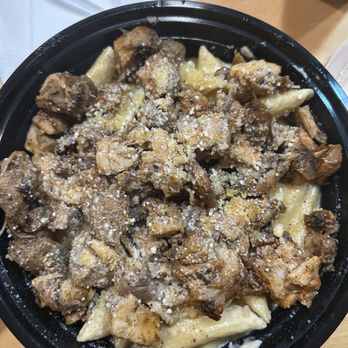 Traphouse Caribbean - Rasta Pasta with jerk chicken and shrimp. My shrimp we're on the side. - A black bowl holds pasta topped with cooked chicken pieces, grated cheese, and a sprinkle of cheese, served on a wooden table. - Caribbean Near Me - Austin, Texas