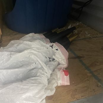 Extra Space Storage - Black and gold objects, possibly umbrellas or sticks, are wrapped in white plastic and placed on a wooden floor near a wall and a piece of furniture. - Self Storage Near Me - Boston, Massachusetts