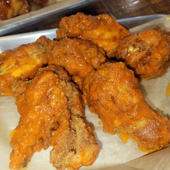 Bobby Mcgee’s - Buffalo wings - A close-up of buffalo chicken wings covered in orange sauce, served on a tray with small containers of dipping sauce. - Bars Near Me - Fort Wayne, Indiana