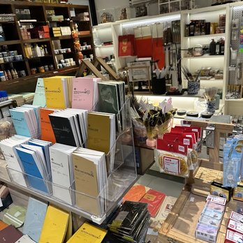 Eglance Bookstore - A bookstore shelf features a variety of notebooks, stationery, and art supplies, with shelves of art tools and decorative items in the background. - Books, Mags, Music & Video Near Me - Flushing, New York
