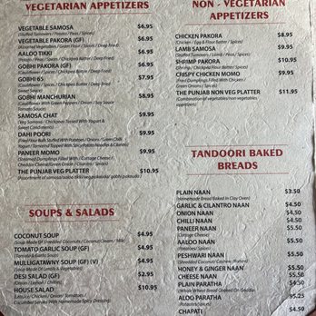 The Punjab - Menu - The menu features sections for appetizers, soups, salads, and baked breads. Vegetarian appetizers include GOBHI PAKORA, AA LO TIKKI, and SAMOSA CHAT, with prices ranging from $6.95 to $9.95. Non-vegetarian options include CHICKEN PAKORA, LAMB SAMOSA, and CRISPY CHICKEN MOM, priced between $8.95 and $11.95. Soups include coconut, tomato garlic, and mulligatawny, each costing $4.95, while salads include desi salad and house salad. Baked breads such as plain naan, garlic naan, and onion naan are priced from $3.50 to $4.50, with various other options like chapati and roti also listed. The menu is printed on textured paper with a red and beige color scheme. - Indian Near Me - Johnston, Rhode Island