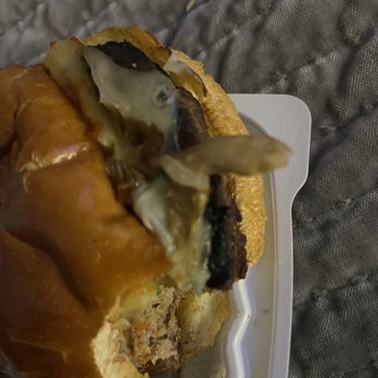 3rd Base Bar & Grill - Burnt char and burger was hammered (overcooked). Wings were also had old taste. Called owner. Left messages..No return call. - A close-up of a burger with melted cheese, toppings, and a bun, served on a white tray, with a quilted fabric background. - Sports Bars Near Me - Olean, New York