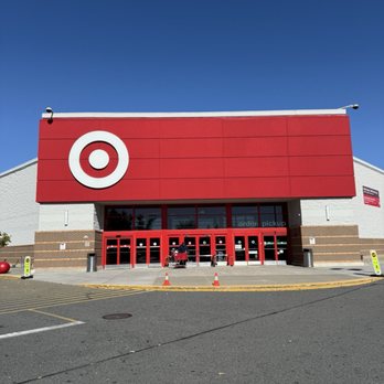 Target - The image shows the front exterior of a Target store located in Hackensack, New Jersey. The building has a large red sign with the Target logo above the entrance, which consists of multiple red doors. The area in front of the store includes a parking lot with some traffic cones and signs, and the sky above is clear and blue. - Department Stores Near Me - Hackensack, New Jersey