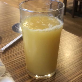 IHOP - Water, masking itself as orange juice ... - A tall glass filled with orange juice is placed on a wooden table in a restaurant, with chairs and a warm interior in the background. - Breakfast & Brunch Near Me - Saco, Maine
