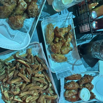 St James Irish Pub - Half priced wings (secret sauce garlic parm mixed with one of their buffalo flavors), buffaque and Asian sticky with fries with Cajun rub - Fried chicken wings with various sauces and French fries are served on metal trays lined with newspaper-style paper at a restaurant. - Irish Near Me - Fall River, Massachusetts