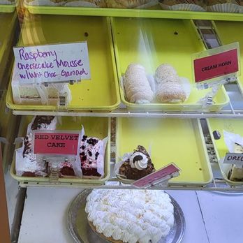 Allegretti's Bakery - A bakery display case contains assorted cakes and desserts, such as rum balls, German chocolate cake, raspberry mousse, and cream horn, with handwritten labels. - Bakeries Near Me - Norridge, Illinois