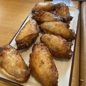 Mom's Dumpling - A rectangular ceramic plate holds several fried chicken wings with a golden-brown, crispy exterior. The plate is placed on a wooden table, with a glass of water and a black napkin visible in the background. The setting appears to be a casual dining environment, likely a restaurant specializing in fried foods. - Dim Sum Near Me - Davis, California