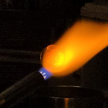 Monadnock Glass Arts - A glassblowing torch with a blue label emits a bright orange flame in a dark setting, likely in a glass art studio. - Art Galleries Near Me - Somerville, Massachusetts