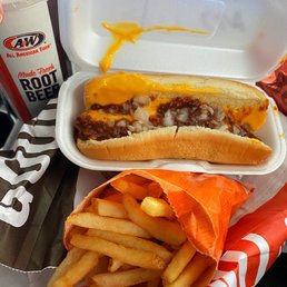 a hot dog and french fries - A fast food meal from A&W includes a hot dog with chili and onions, a side of French fries, and a root beer in a paper cup.