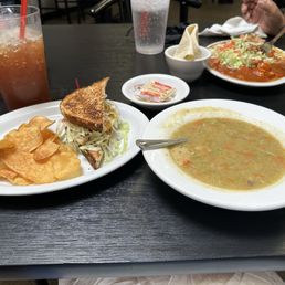 Open Faced Green Chile Burger - A plate with potato chips, a sandwich, and a bowl of soup is on a black table, with drinks and condiments nearby.