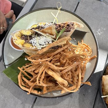 Buen Provecho - Weekend special breakfast burrito - A plate contains two tacos filled with meat, topped with cheese, and garnished with a leaf, alongside fried plantains on a gray outdoor table. - Latin American Near Me - Albuquerque, New Mexico